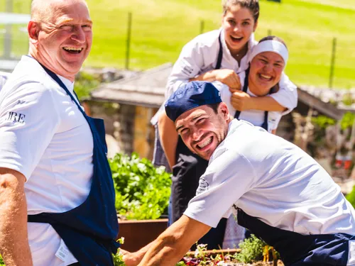 Smiling chefs in uniform harvesting herbs together in a sunny garden